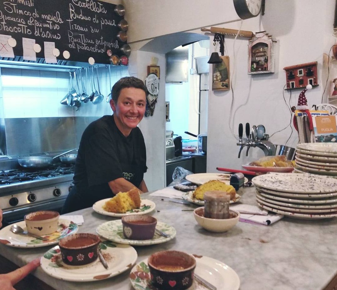Antonella Scatigna nella sua cucina a vista, dietro il bancone con i piatti e la lavagna del menu